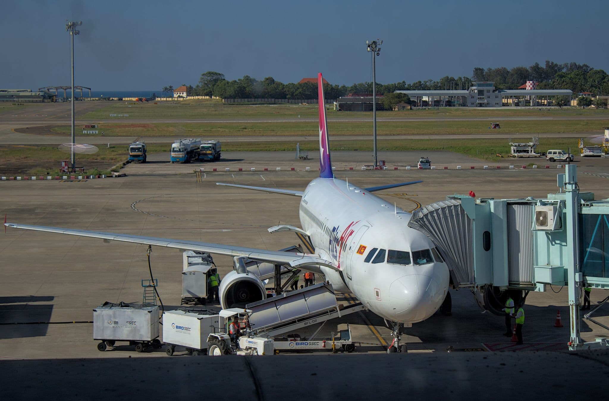 FitsAir Airbus A320 4R-EXR parked at an airport gate with jet bridge attached