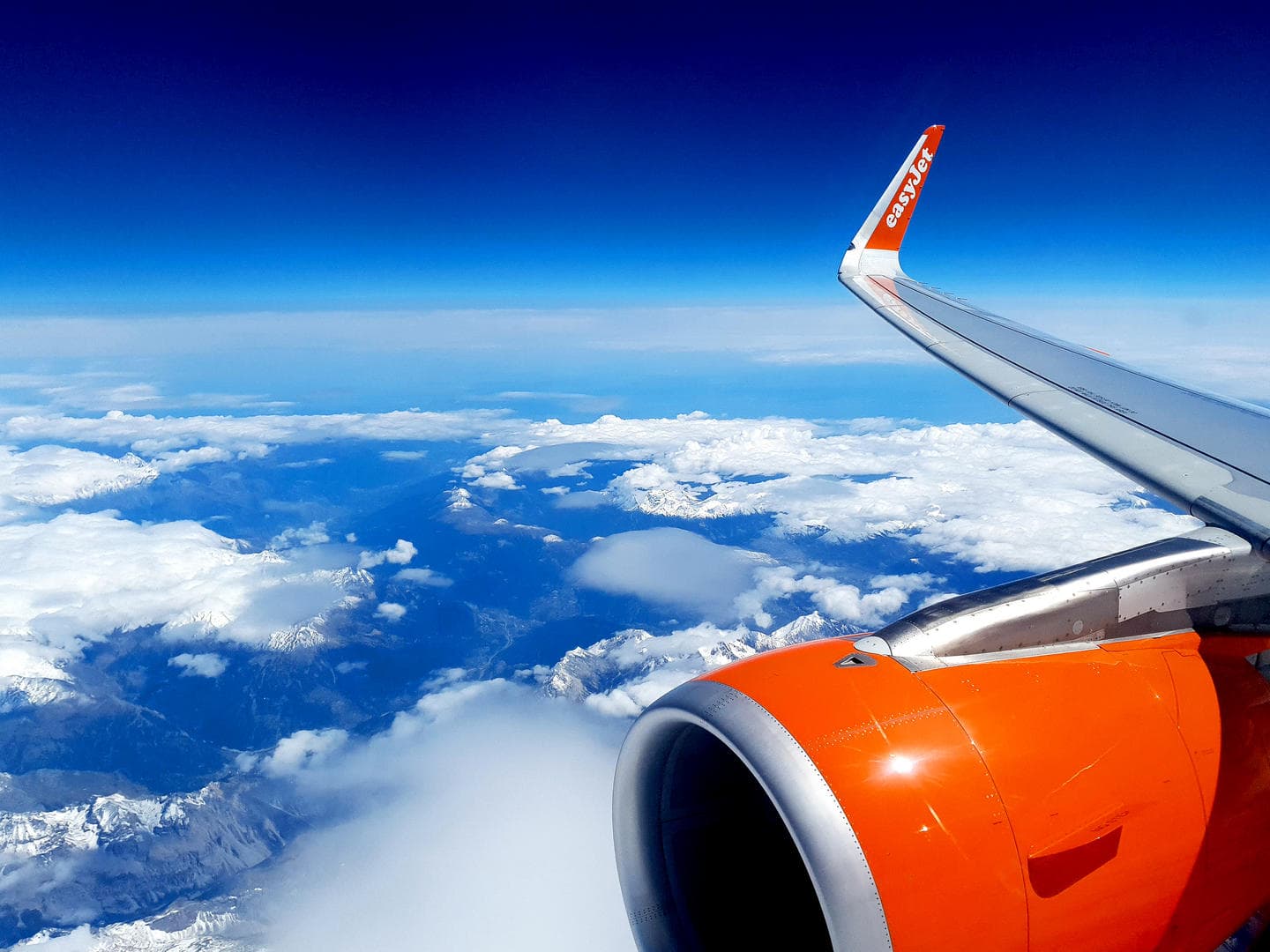 View of an easyJet wing and orange engine above the clouds