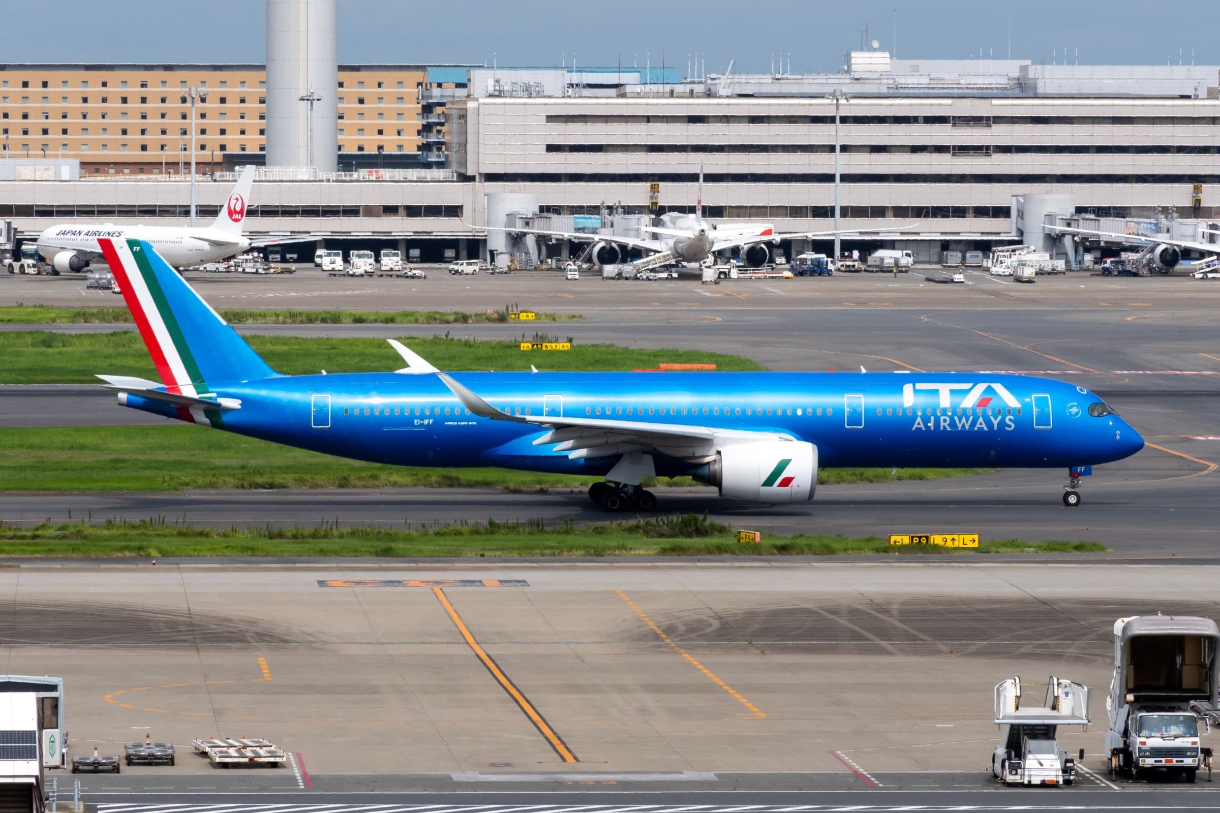 Airbus A350-900 da ITA Airways (EI-IFF) a rolar no Aeroporto de Tóquio-Haneda, com o terminal ao fundo