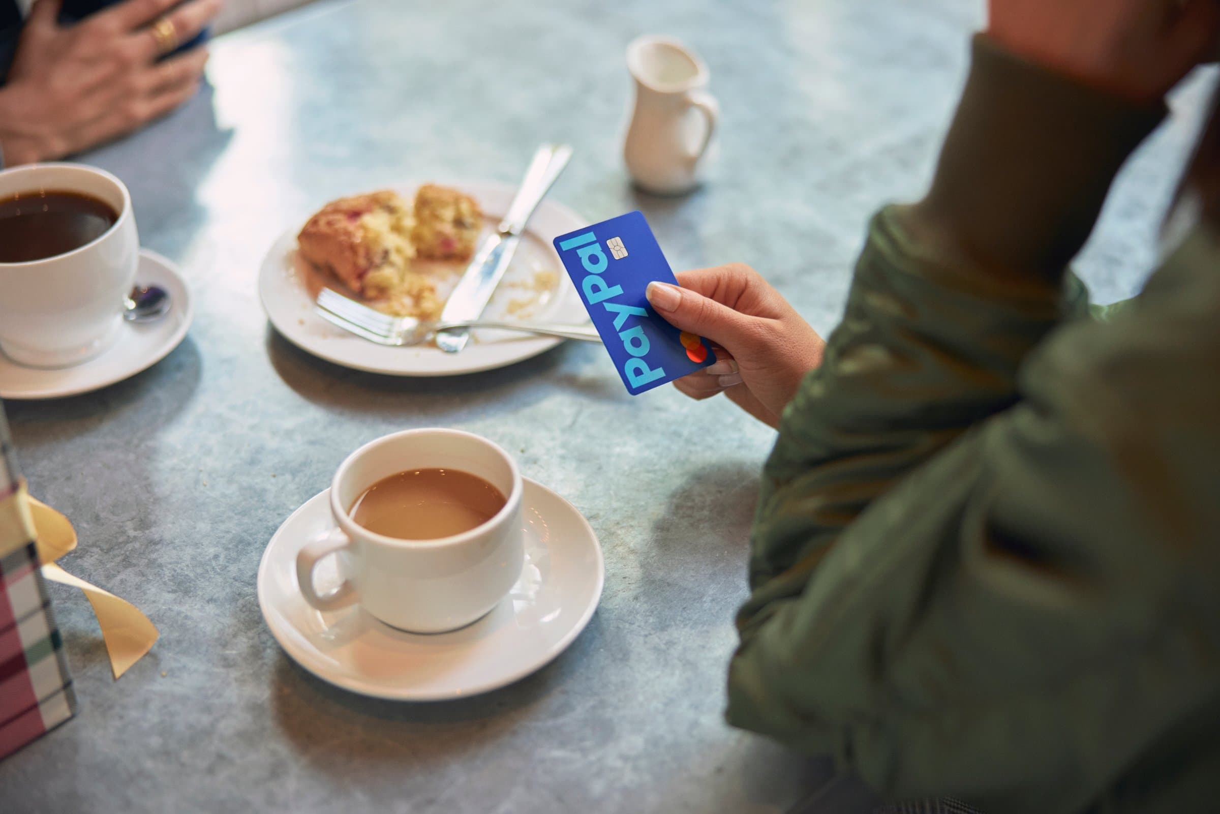 Hand holding a PayPal debit card at a cafe table