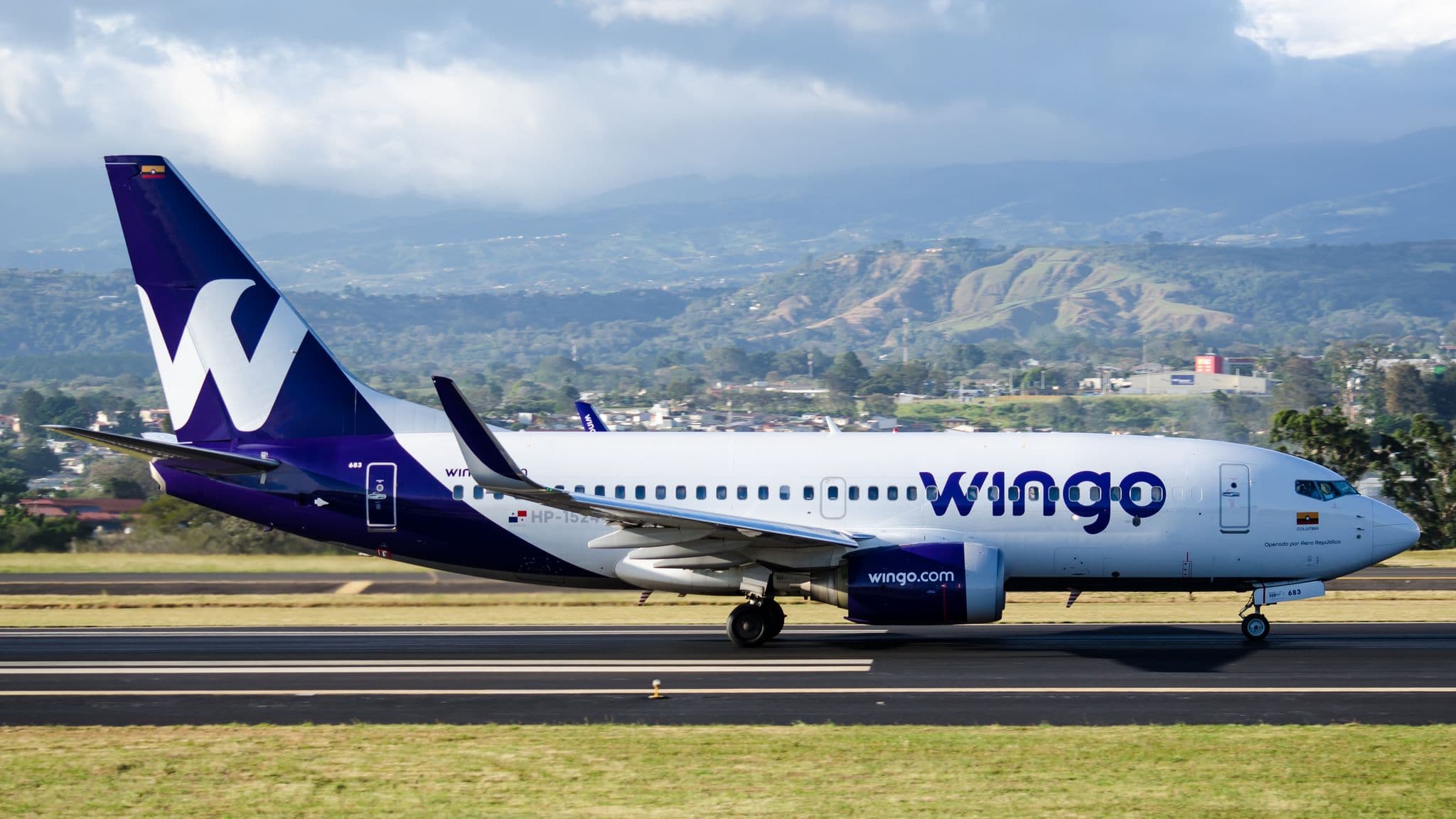 Wingo Boeing 737-700 in purple-and-white livery taxiing with mountains behind