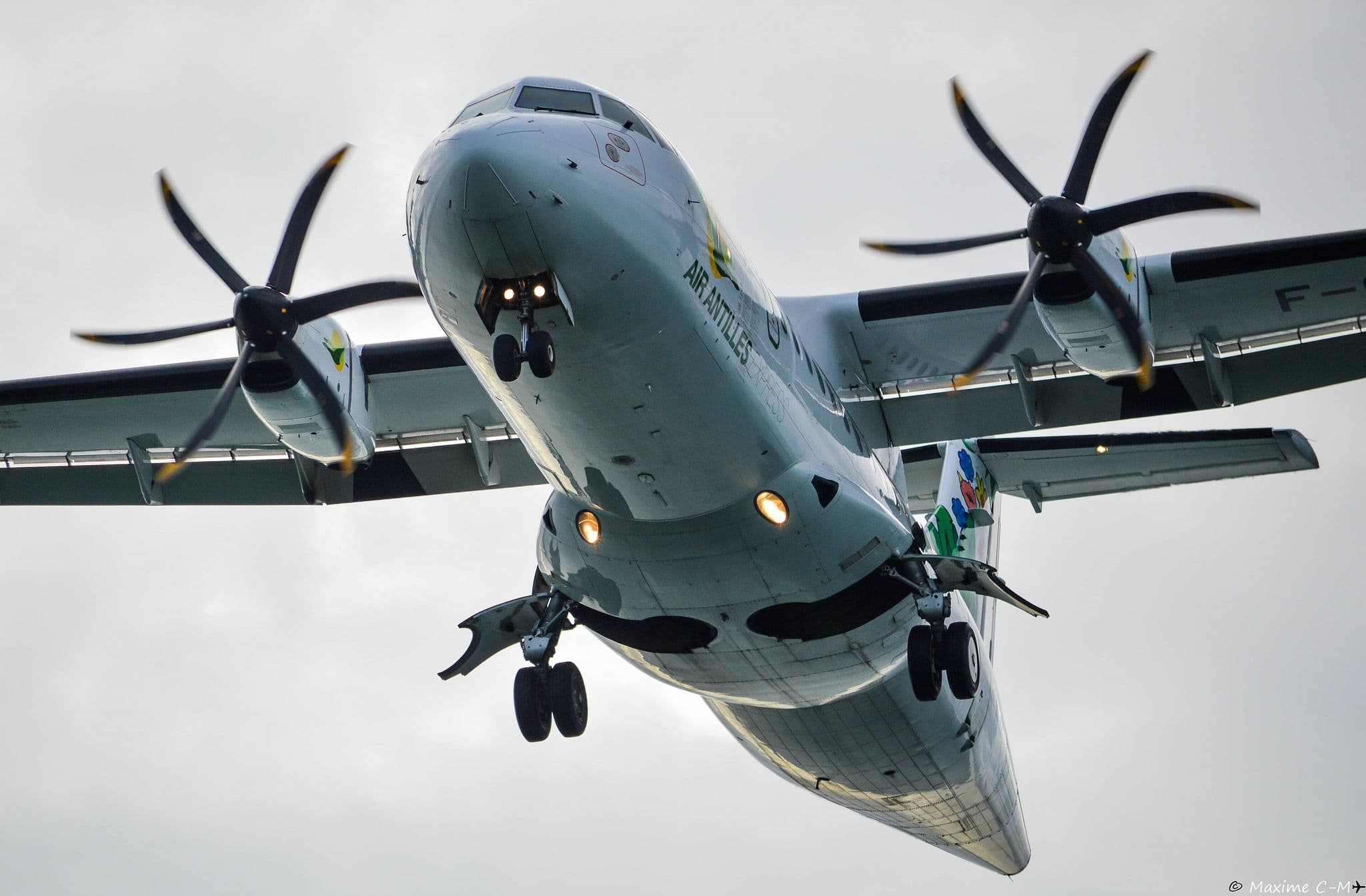 Close-up of an Air Antilles ATR 42-500 from below, propellers spinning as it comes in to land