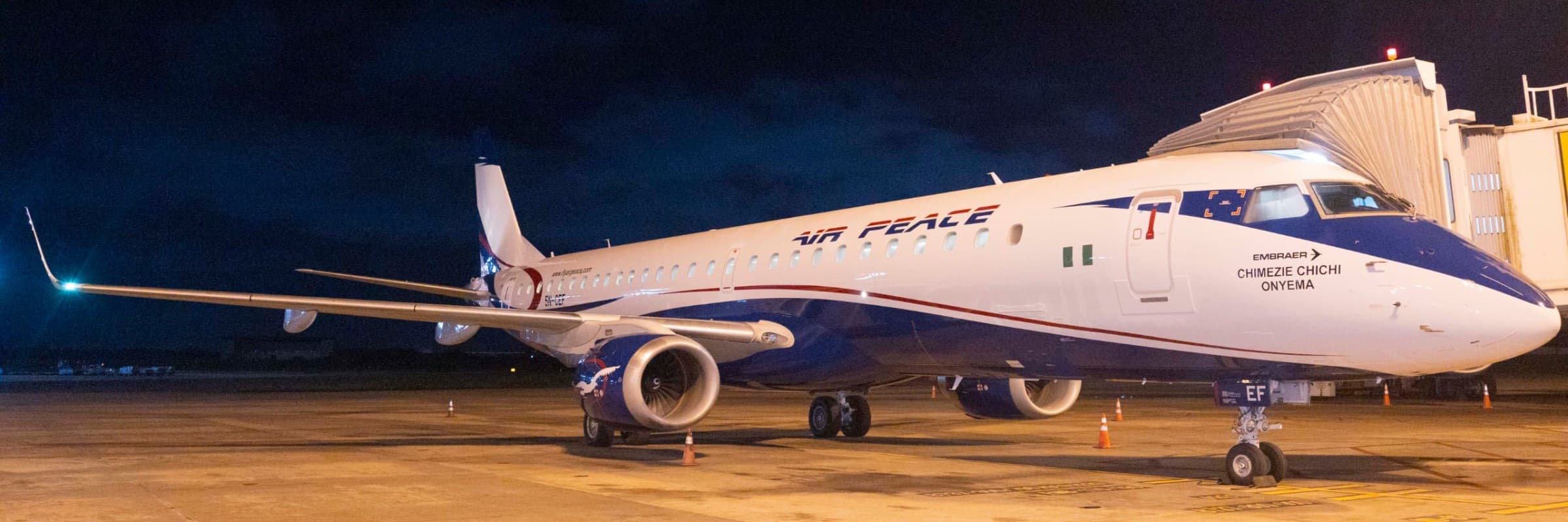 Air Peace Embraer jet parked at an airport gate at night