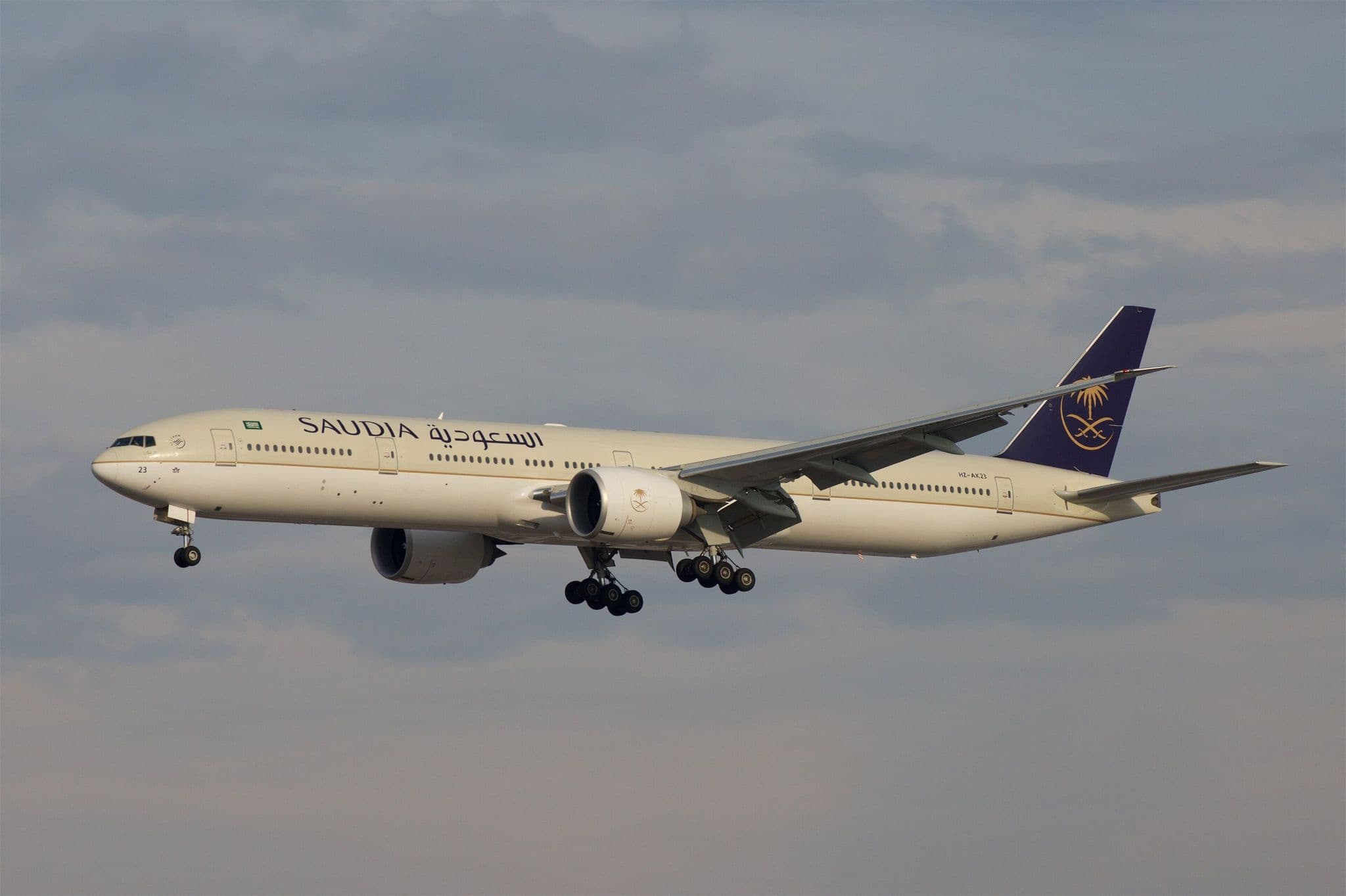 Saudia Boeing 777-300ER HZ-AK23 on approach with landing gear down against a grey sky