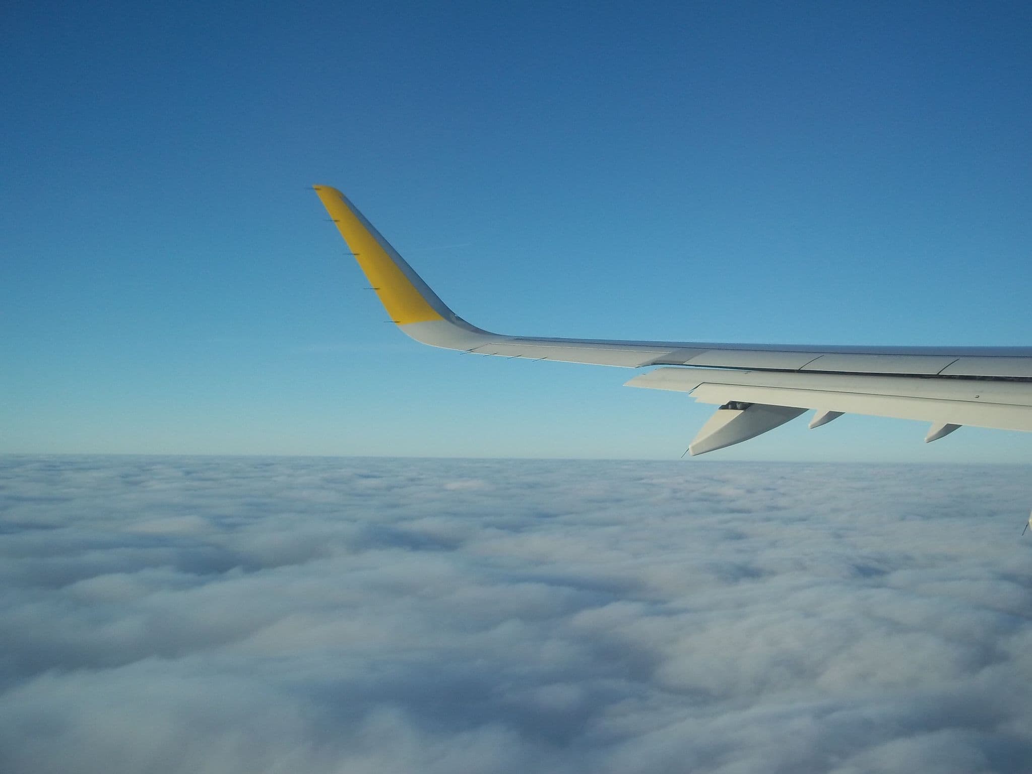 雲の上を飛ぶVueling Airbus機の窓から見た、先端が黄色い翼