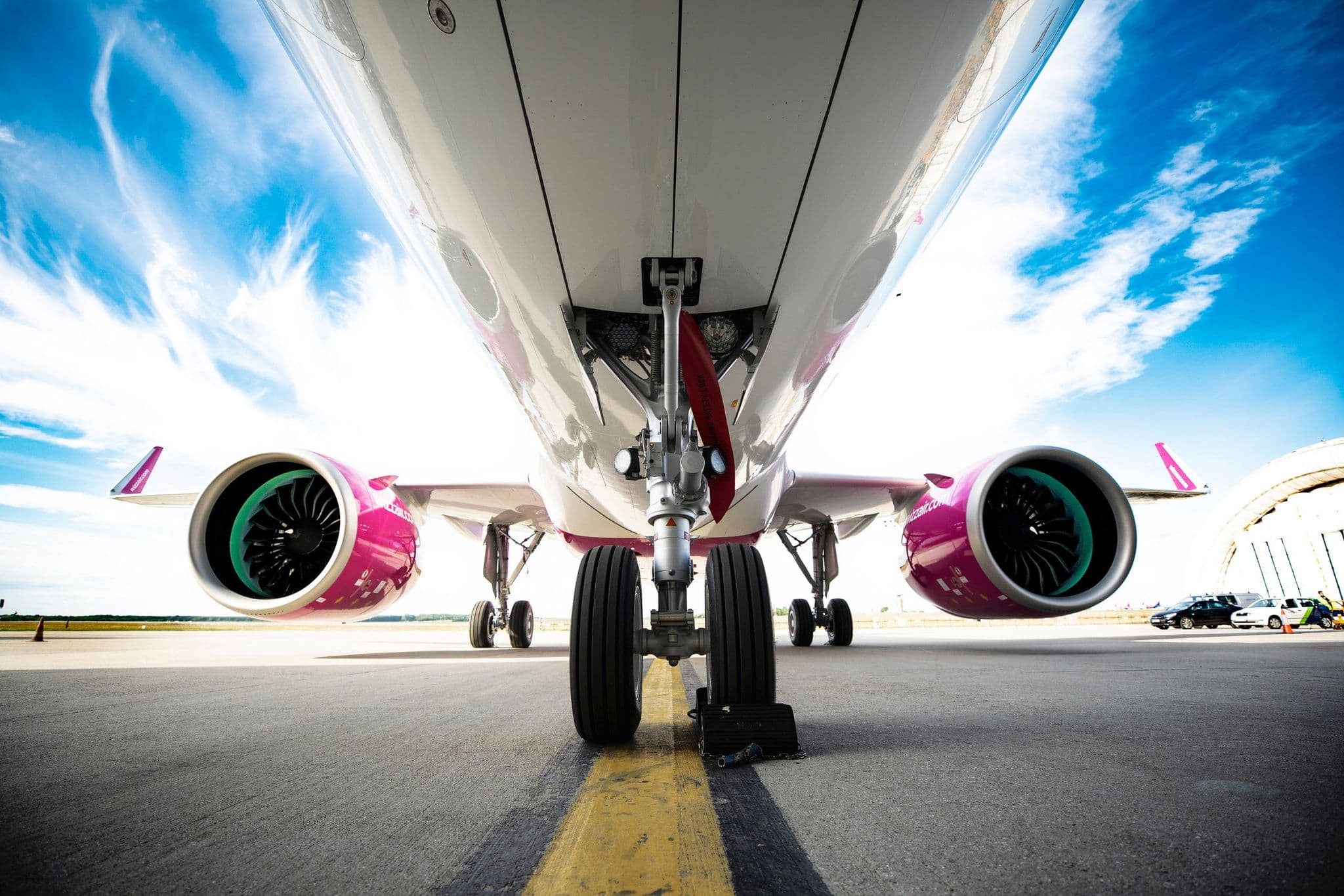 從 Wizz Air Airbus A320neo 機腹下方拍攝,可見引擎與粉紅色塗裝